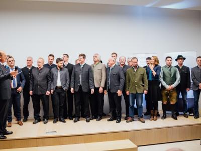 Das Team vom Pelhamer See mit über 20 Personen auf der Bühne im Staatsministerium, die meisten schauen nach links zum Moderator.