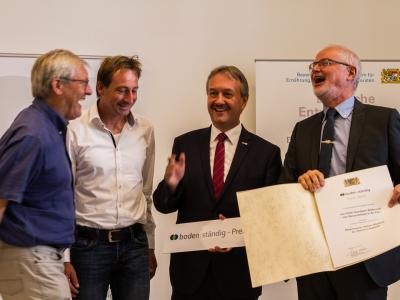 Ministerialdirigent Maximilian Geierhos (rechts) versteht sich offensichtlich gut mit dem Gewinner Herbert Blascheck (2.v.r) und seinem Unterstützerteam. © Büttner/BZA
